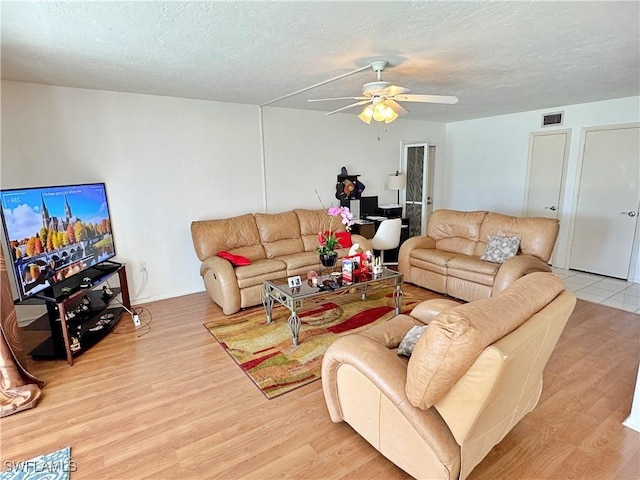 living room with ceiling fan, a textured ceiling, and light hardwood / wood-style floors