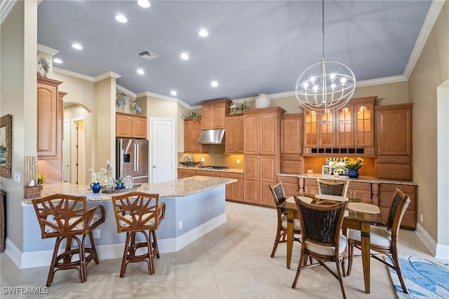 kitchen with a kitchen bar, light stone counters, crown molding, hanging light fixtures, and appliances with stainless steel finishes