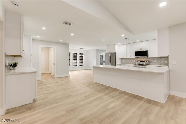 kitchen featuring appliances with stainless steel finishes, white cabinetry, decorative backsplash, kitchen peninsula, and light wood-type flooring