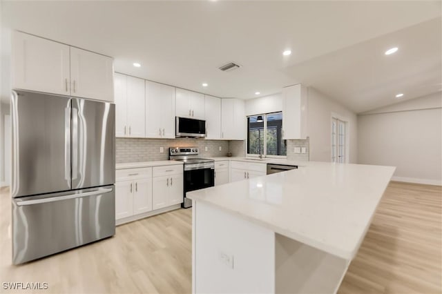 kitchen with tasteful backsplash, light wood-type flooring, appliances with stainless steel finishes, kitchen peninsula, and white cabinets