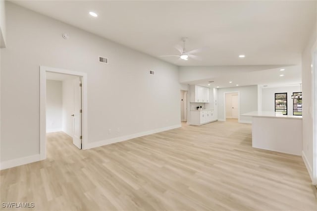 unfurnished living room with ceiling fan, vaulted ceiling, and light wood-type flooring