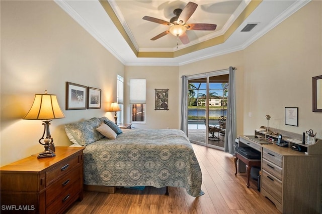 bedroom with ceiling fan, a tray ceiling, ornamental molding, access to outside, and light wood-type flooring