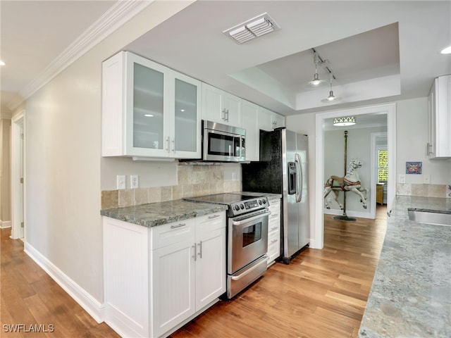 kitchen featuring appliances with stainless steel finishes, white cabinetry, light stone counters, a raised ceiling, and light hardwood / wood-style flooring