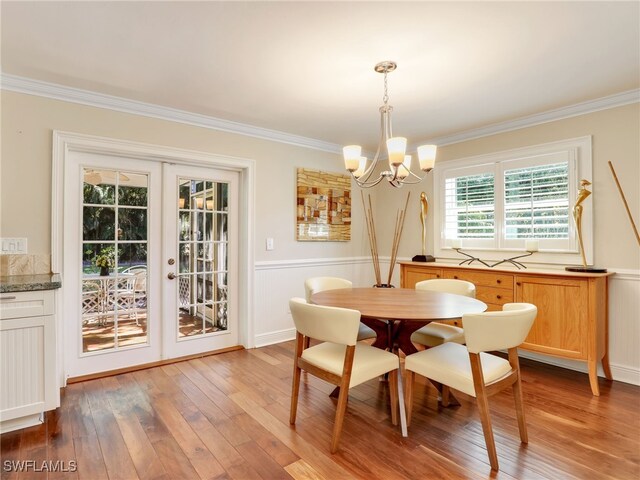 dining area with an inviting chandelier, wood-type flooring, ornamental molding, and french doors