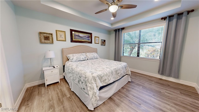 bedroom with a raised ceiling, ceiling fan, and light hardwood / wood-style flooring