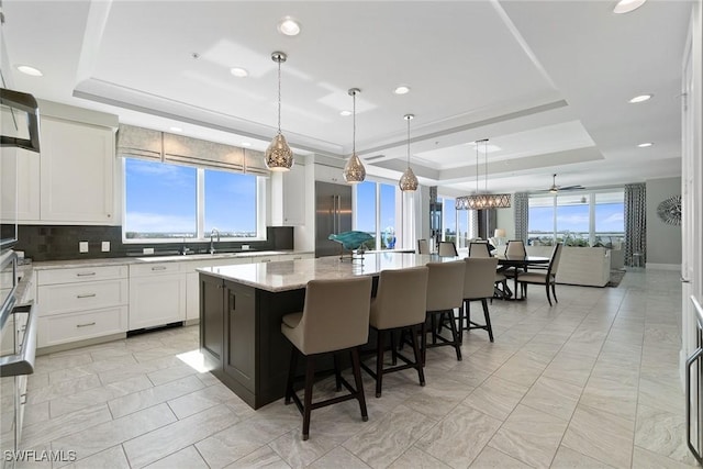 kitchen featuring pendant lighting, a tray ceiling, a center island, and white cabinets