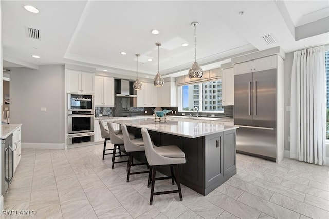 kitchen with wall chimney exhaust hood, sink, a center island, appliances with stainless steel finishes, and a tray ceiling