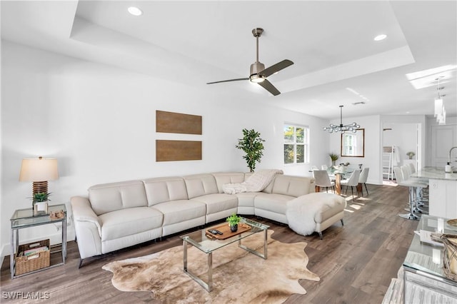 living room featuring dark hardwood / wood-style floors, ceiling fan with notable chandelier, and a tray ceiling