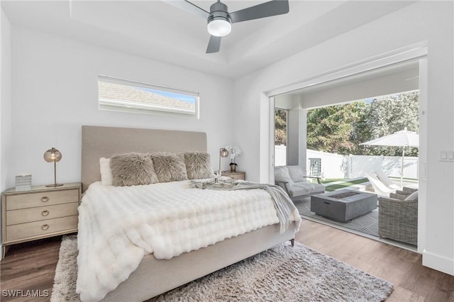 bedroom with ceiling fan, access to outside, dark hardwood / wood-style flooring, and a tray ceiling