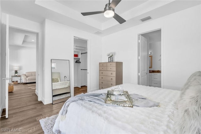 bedroom featuring hardwood / wood-style floors, connected bathroom, a raised ceiling, a walk in closet, and a closet