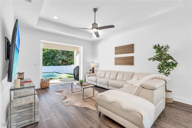 living room featuring ceiling fan, dark hardwood / wood-style floors, and a raised ceiling