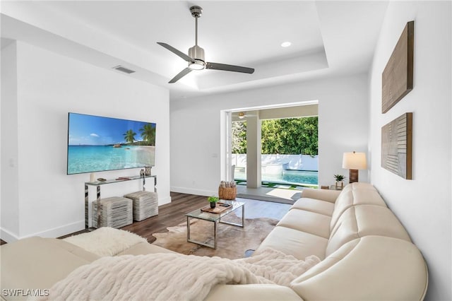 living room with hardwood / wood-style flooring, ceiling fan, and a tray ceiling