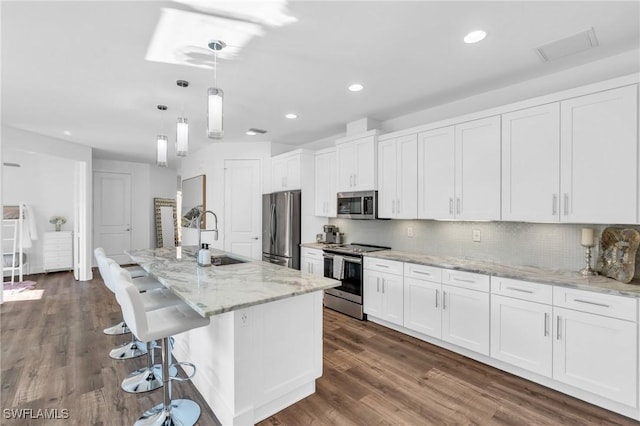 kitchen with sink, pendant lighting, stainless steel appliances, a kitchen island with sink, and white cabinets