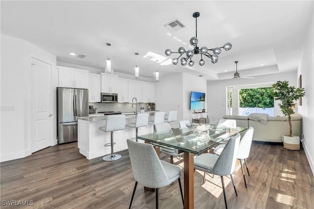 dining space featuring a raised ceiling, sink, dark hardwood / wood-style floors, and ceiling fan with notable chandelier