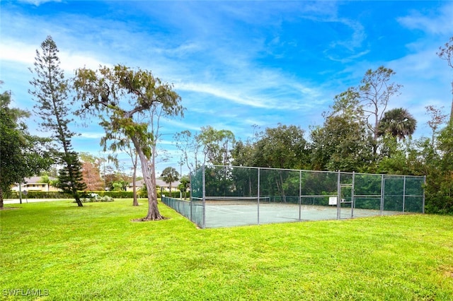 view of tennis court with a yard and fence