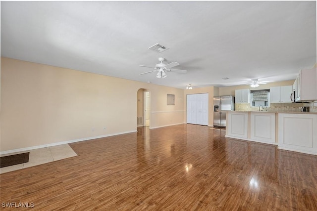 unfurnished living room featuring hardwood / wood-style floors, sink, and ceiling fan