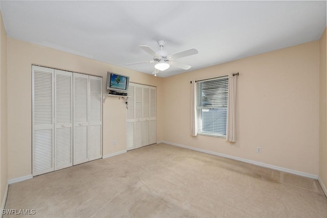 unfurnished bedroom featuring ceiling fan, light carpet, and two closets