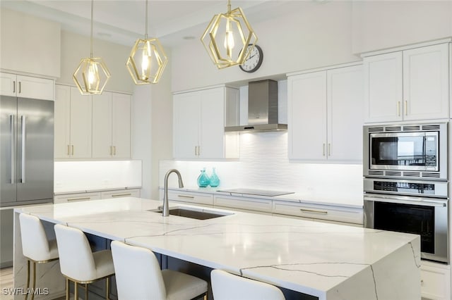 kitchen featuring sink, a kitchen island with sink, built in appliances, light stone countertops, and wall chimney exhaust hood