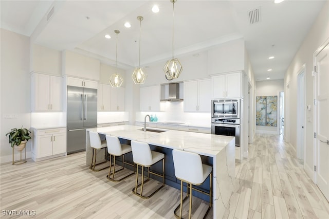 kitchen with a large island, sink, built in appliances, light stone countertops, and white cabinets