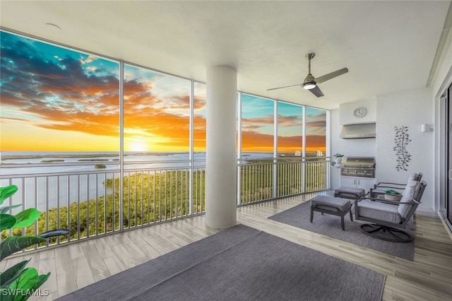 sunroom with ceiling fan and a water view