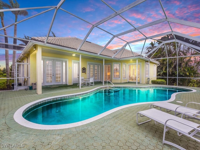 pool at dusk with a patio, glass enclosure, and french doors