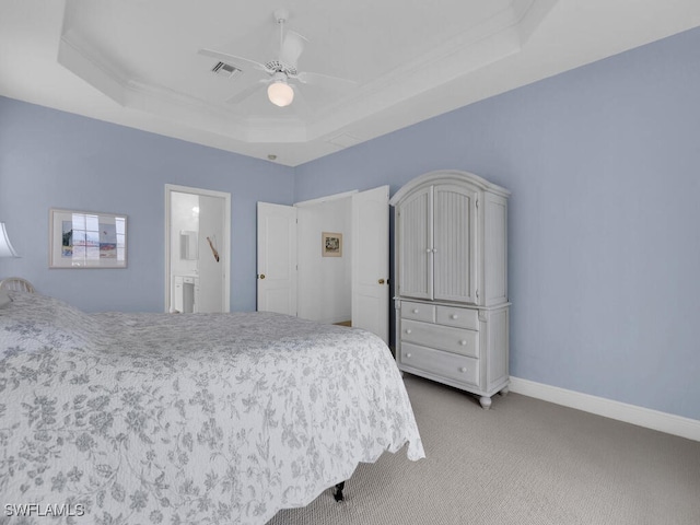 carpeted bedroom featuring crown molding, a tray ceiling, ensuite bath, and ceiling fan