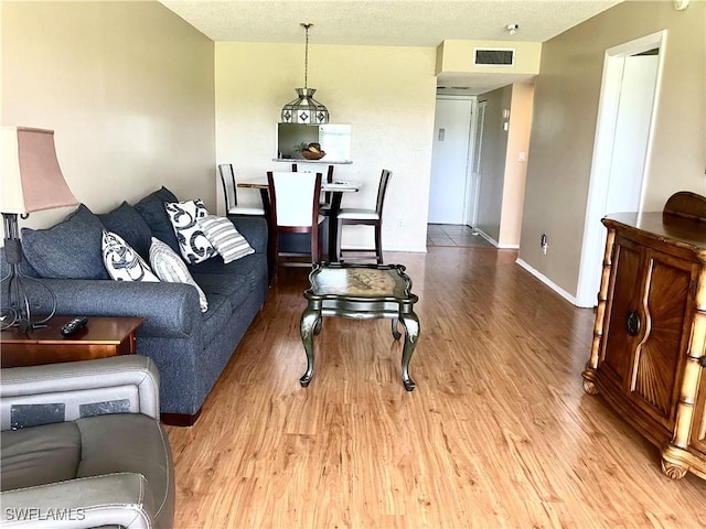 living room featuring baseboards, a textured ceiling, visible vents, and wood finished floors