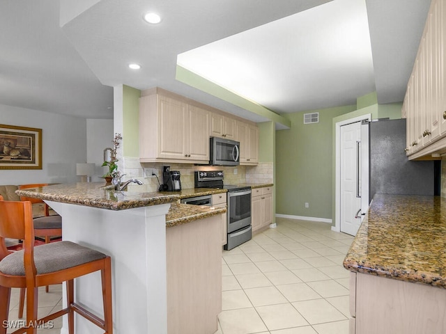 kitchen featuring a breakfast bar area, backsplash, dark stone counters, kitchen peninsula, and stainless steel appliances