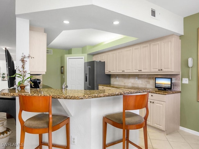 kitchen with a kitchen breakfast bar, high quality fridge, kitchen peninsula, and dark stone counters