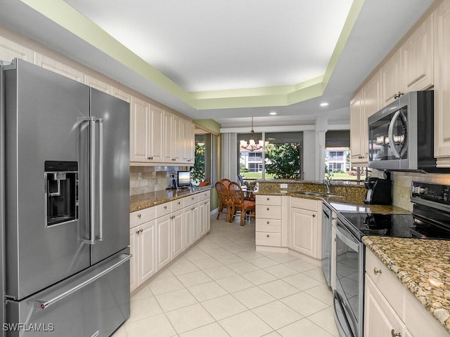 kitchen featuring sink, dark stone counters, a raised ceiling, stainless steel appliances, and backsplash