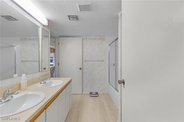 bathroom featuring wood-type flooring, combined bath / shower with glass door, vanity, and a textured ceiling