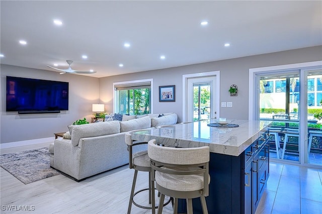 kitchen with ceiling fan, a kitchen island, light wood-type flooring, and a kitchen breakfast bar