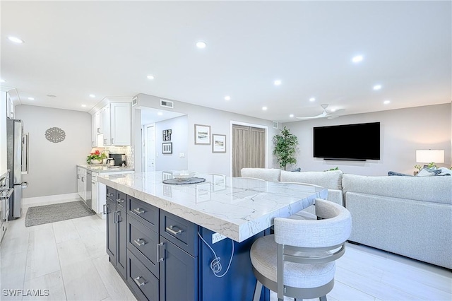 kitchen with a kitchen bar, light stone counters, a center island, stainless steel appliances, and white cabinets