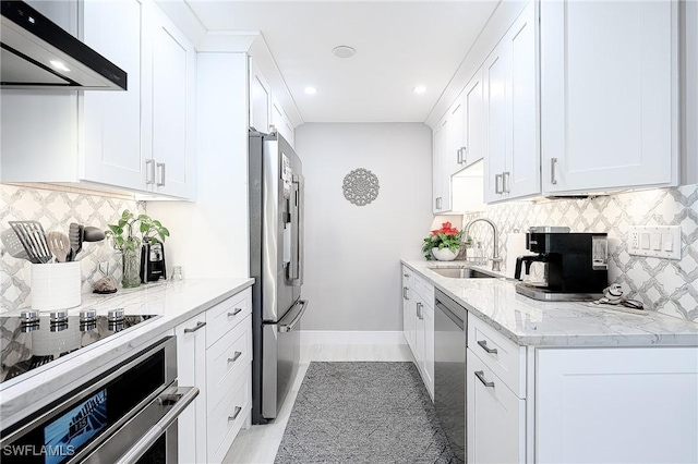 kitchen with sink, light stone counters, appliances with stainless steel finishes, wall chimney range hood, and white cabinets