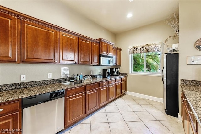 kitchen with stainless steel appliances, sink, light tile patterned floors, and dark stone counters