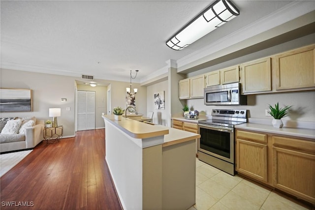 kitchen featuring sink, hanging light fixtures, ornamental molding, stainless steel appliances, and a center island with sink