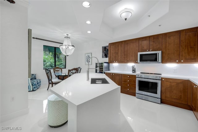 kitchen featuring appliances with stainless steel finishes, sink, hanging light fixtures, a kitchen island with sink, and a raised ceiling