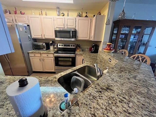 kitchen featuring a peninsula, appliances with stainless steel finishes, a sink, and light stone countertops