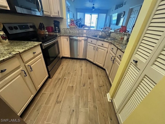 kitchen with light wood-type flooring, light stone counters, stainless steel appliances, and a sink