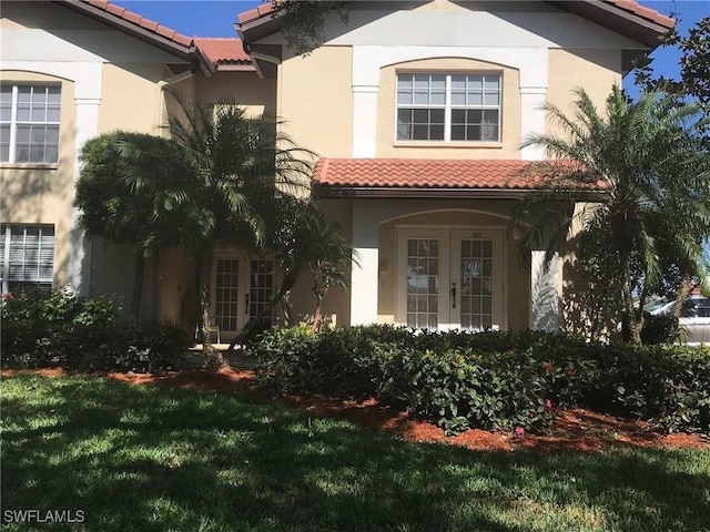 view of front of house with stucco siding, a tiled roof, and french doors