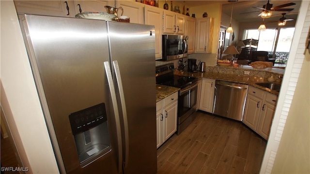 kitchen with ceiling fan, dark wood-type flooring, appliances with stainless steel finishes, dark stone counters, and tasteful backsplash