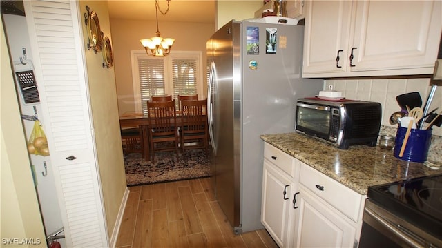 kitchen featuring tasteful backsplash, wood finished floors, freestanding refrigerator, an inviting chandelier, and white cabinetry