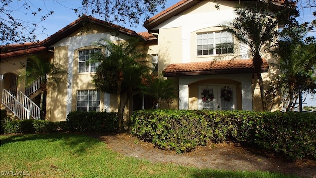 mediterranean / spanish-style home with a tiled roof, stairway, a front yard, and stucco siding