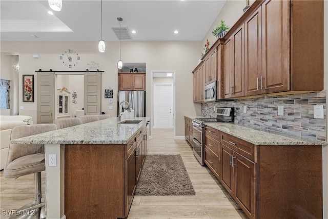 kitchen with sink, decorative light fixtures, a large island with sink, appliances with stainless steel finishes, and a barn door