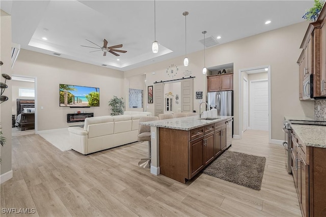 kitchen featuring appliances with stainless steel finishes, hanging light fixtures, a kitchen island with sink, a tray ceiling, and a barn door