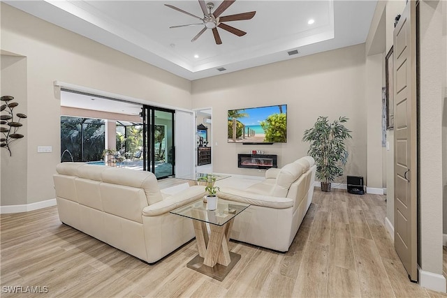 living room featuring ceiling fan, a raised ceiling, a high ceiling, and light wood-type flooring