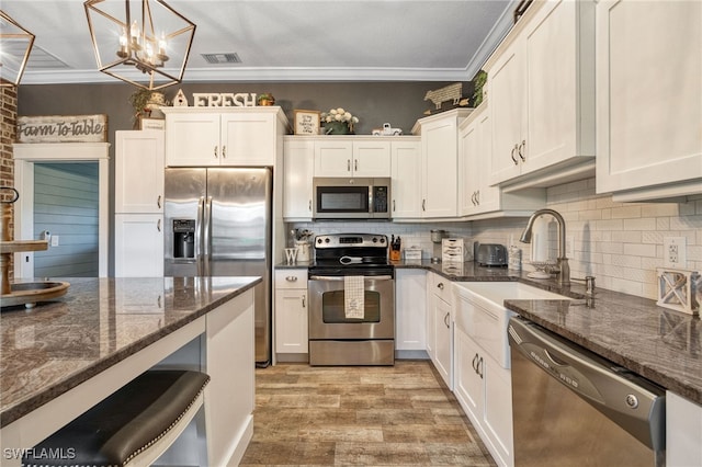 kitchen with white cabinets, stainless steel appliances, hanging light fixtures, and dark stone counters