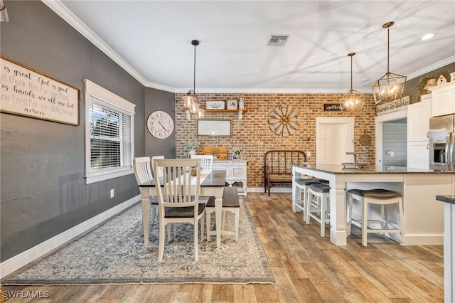 dining room with crown molding, brick wall, and light hardwood / wood-style floors