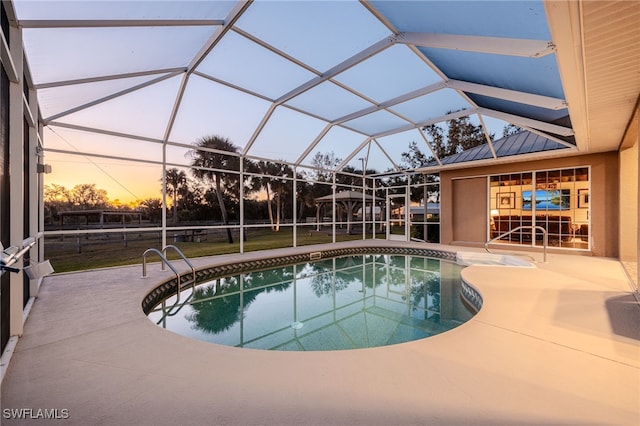 pool at dusk featuring a lanai and a patio area