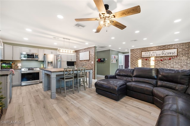 living room featuring light hardwood / wood-style flooring, ornamental molding, ceiling fan, and brick wall